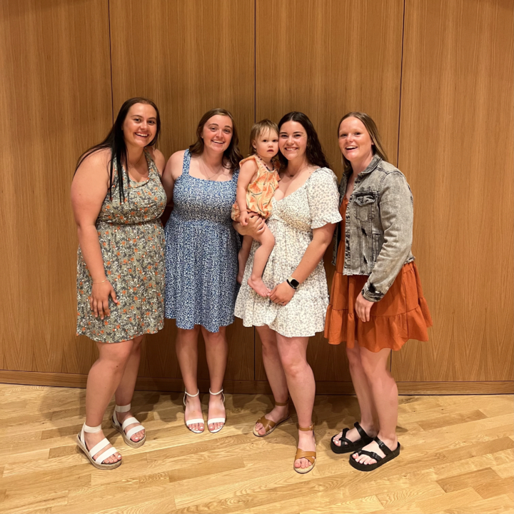 Rebecca Bohrer smiling at the camera with three female students and her daughter
