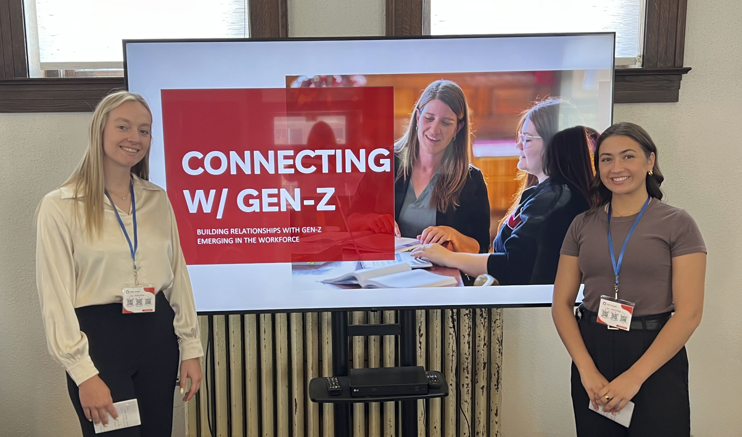 Sarah and classmate standing in front of TV with presentation screen titled Connecting with Gen-Z