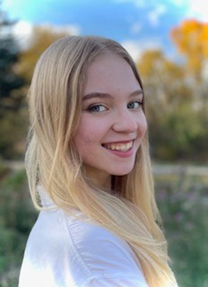 Kalyssa Nelson smiles while posing for a senior photo outdoors in a white shirt