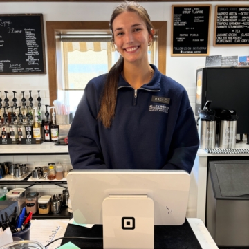 Photo of Macy Fridgen smiling at the camera posing behind a till