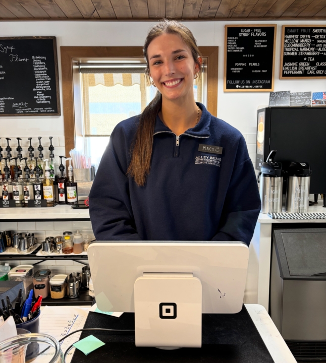 Photo of Macy Fridgen smiling at the camera posing behind a till