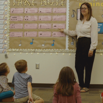 A music educator stands at the front of an elementary school classroom.