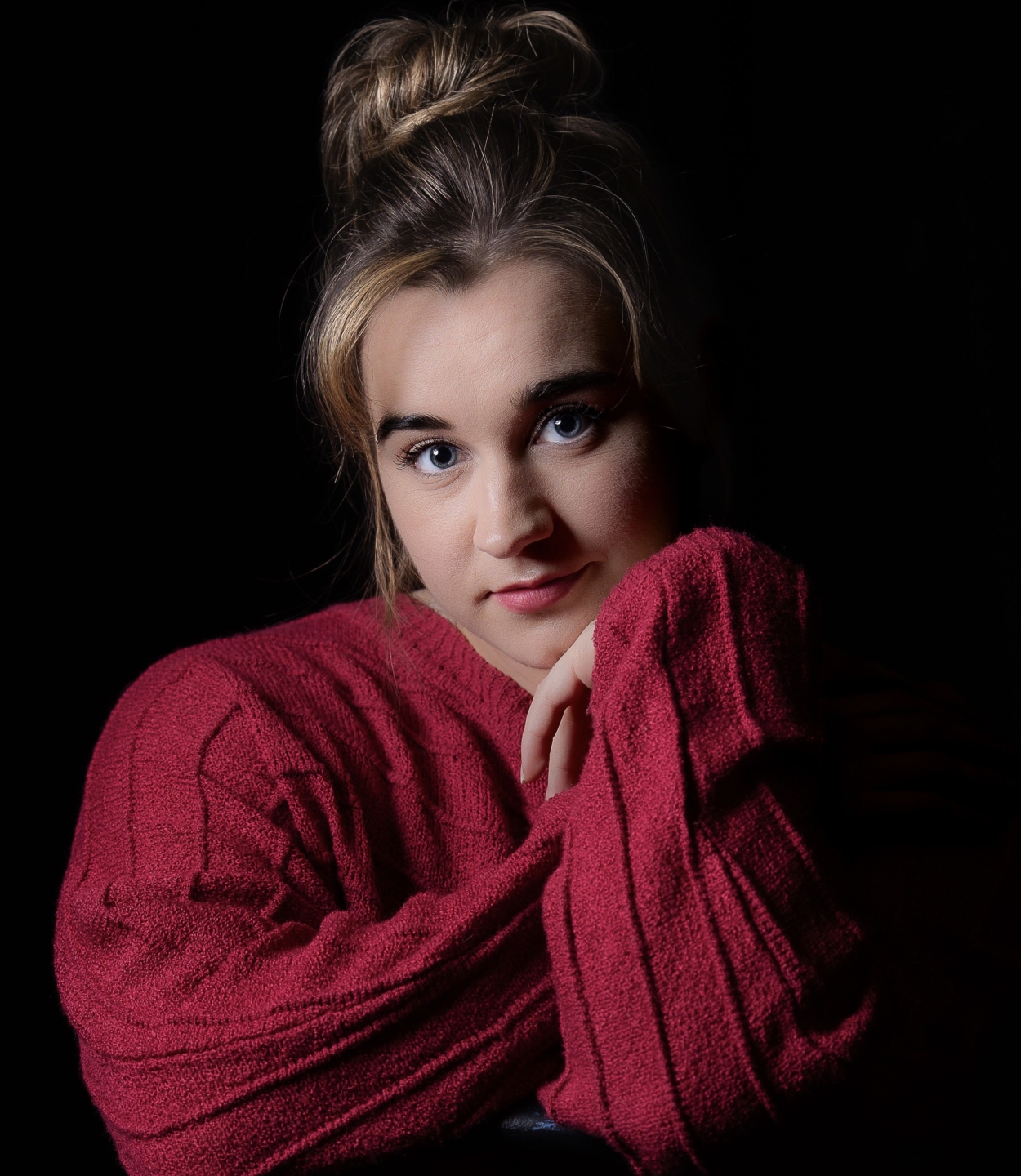 Daryn Imani Nowlin peers at the camera, wearing a red sweater against a black background.