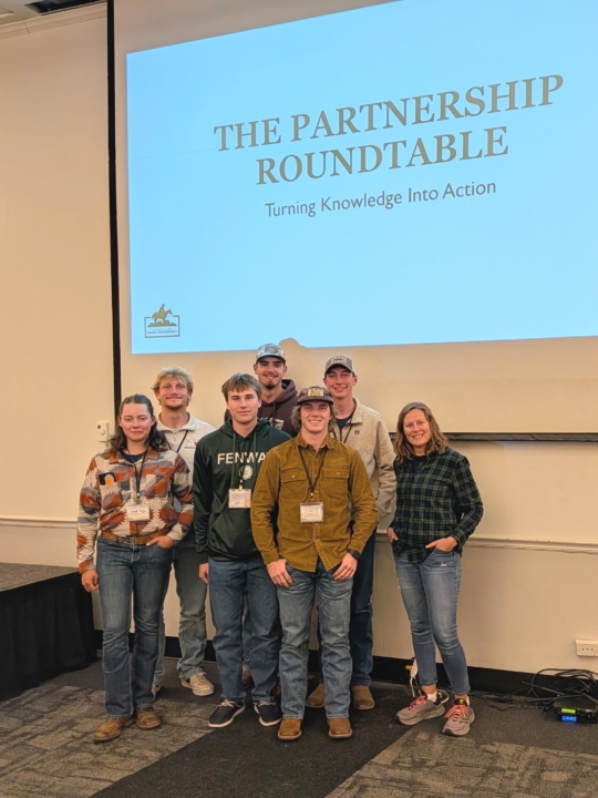 Trista and group of students standing in front of screen that says "The Partnership Roundtable: Turning Knowledge Into Action"