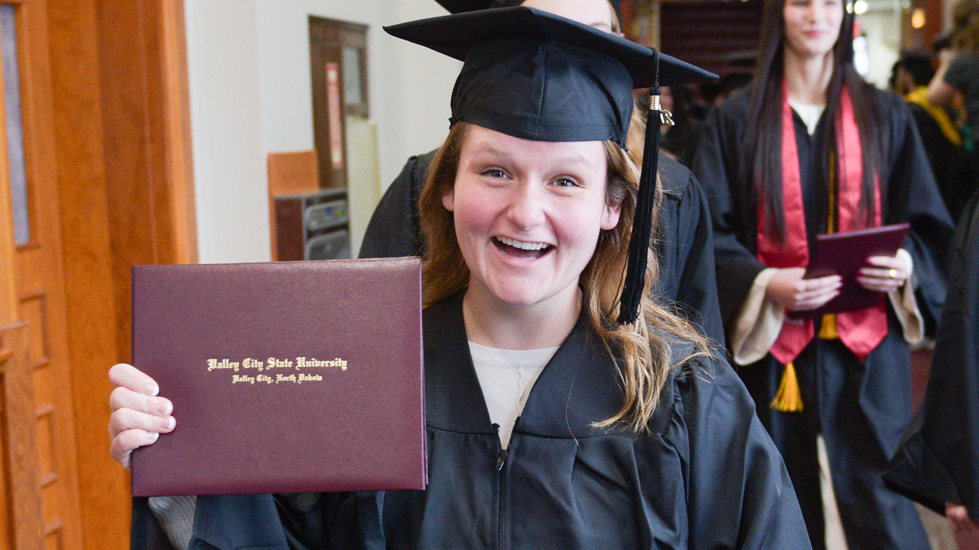 A graduate holds up a diploma and smiles