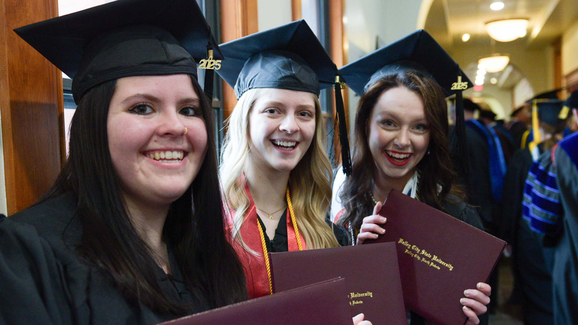 3 female graduates smile and hold up their diplomas