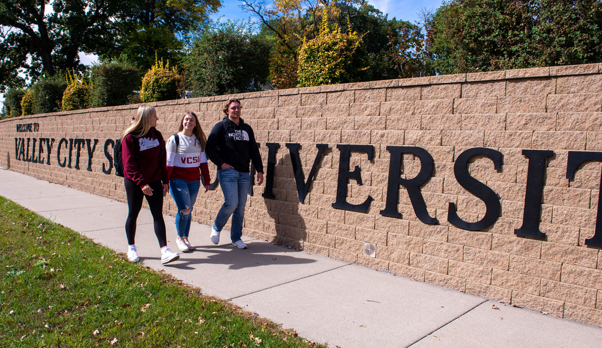 Three students walk near the Welcome to Valley City State University Sign