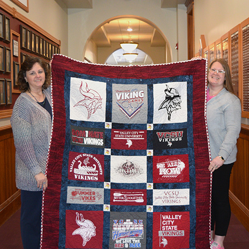 two women holding vcsu themed quilt