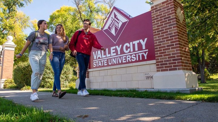 Three students walk near the Valley City State University sign
