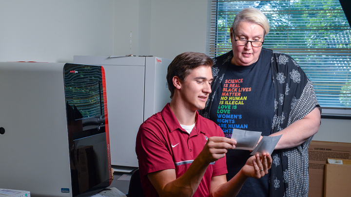 Dr. Hilde van Gijssel converses with a student at a desk in a science lab