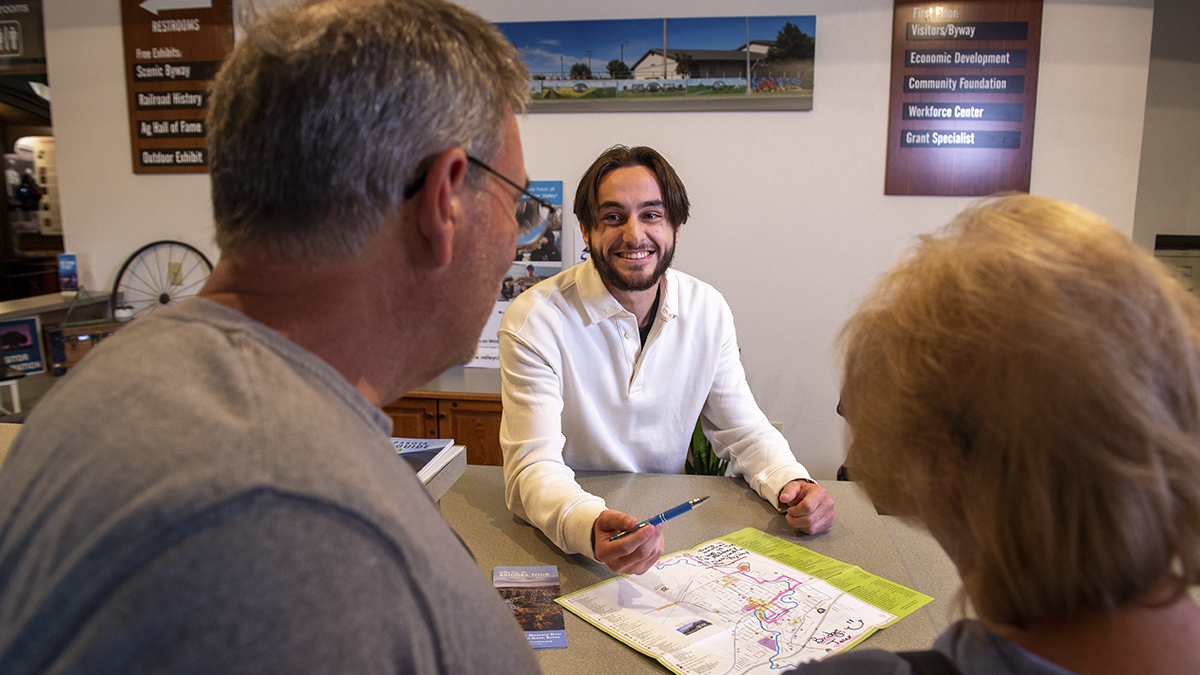 Male student smiling at older couple, showing them a map