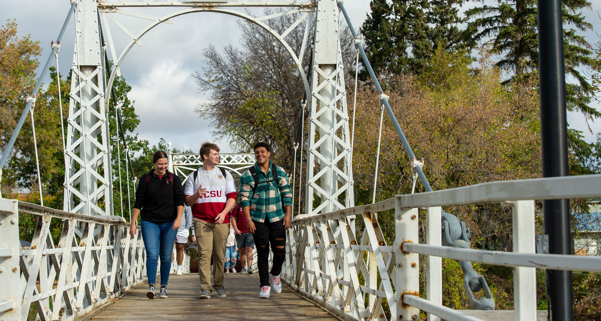 Three students walk across the bridge to campus. 
