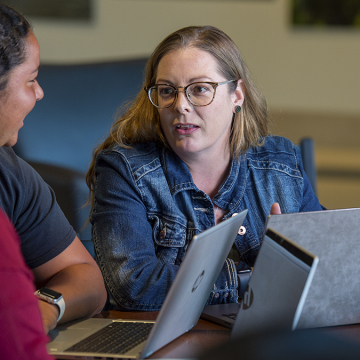 Female student talking to another female student and female professor sitting at a table