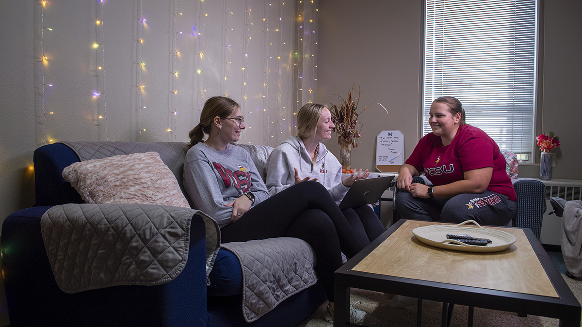 Three female students sitting in the dorm living room talking to each other