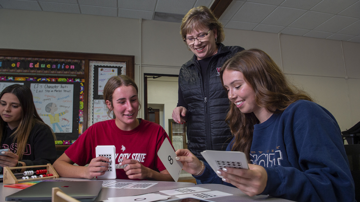 Female teacher talking to two female students who are working on cards