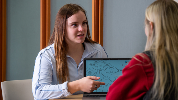 Abby Hill pointing to graphic on a laptop, speaking with other student across the table