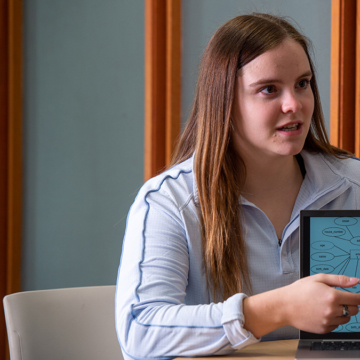 Abby Hill pointing to graphic on a laptop, speaking with other student across the table