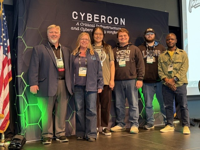 faculty and students standing in front of CyberCon backdrop with green lights